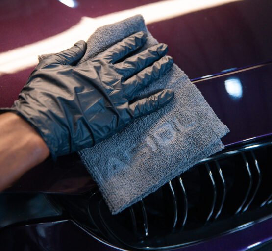 A person dons gloves and a mitt while cleaning a purple car, emphasising the attention to detail in automotive care and maintenance.